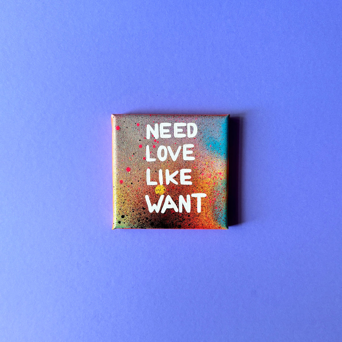 Bunt gesprühtes Kunstwerk mit weißem Schriftzug „Need Love Like Want“.