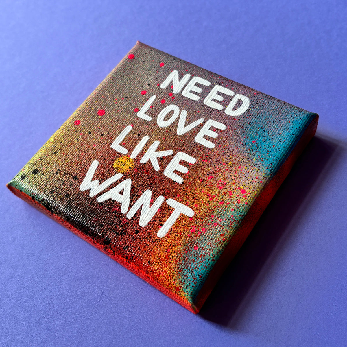 Bunt gesprühtes Kunstwerk mit weißem Schriftzug „Need Love Like Want“.