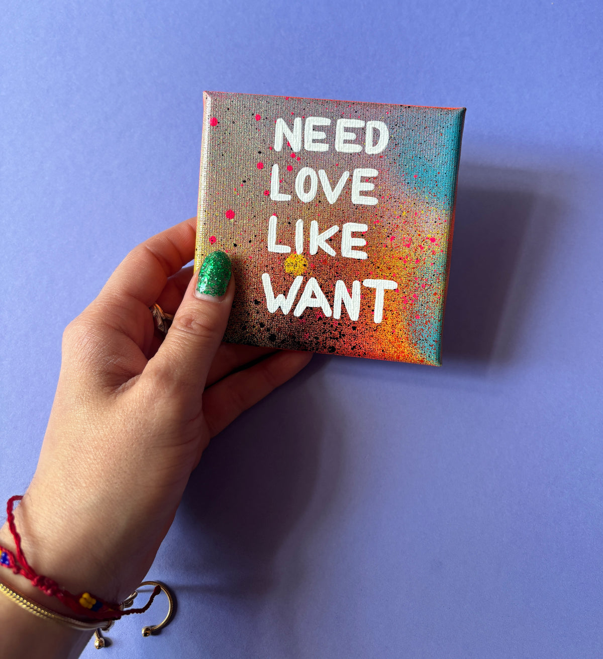 Bunt gesprühtes Kunstwerk mit weißem Schriftzug „Need Love Like Want“. In der Hand haltend. 