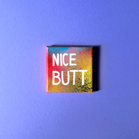 Bunt gesprühtes Kunstwerk mit weißem Schriftzug „Nice Butt“.